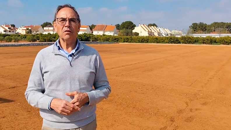 Un hombre de pie en un terreno arenoso con casas al fondo.
