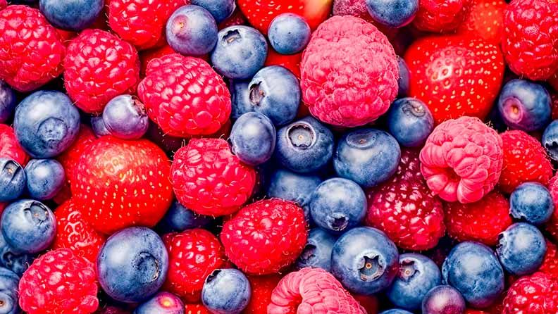La imagen muestra un montón de moras, frambuesas arándanos y una fresa.