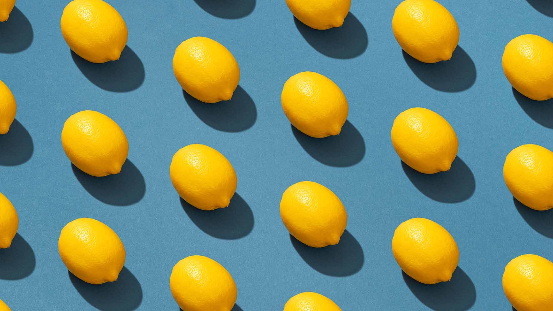 Varios limones amarillos sobre fondo azul con sombras oscuras.