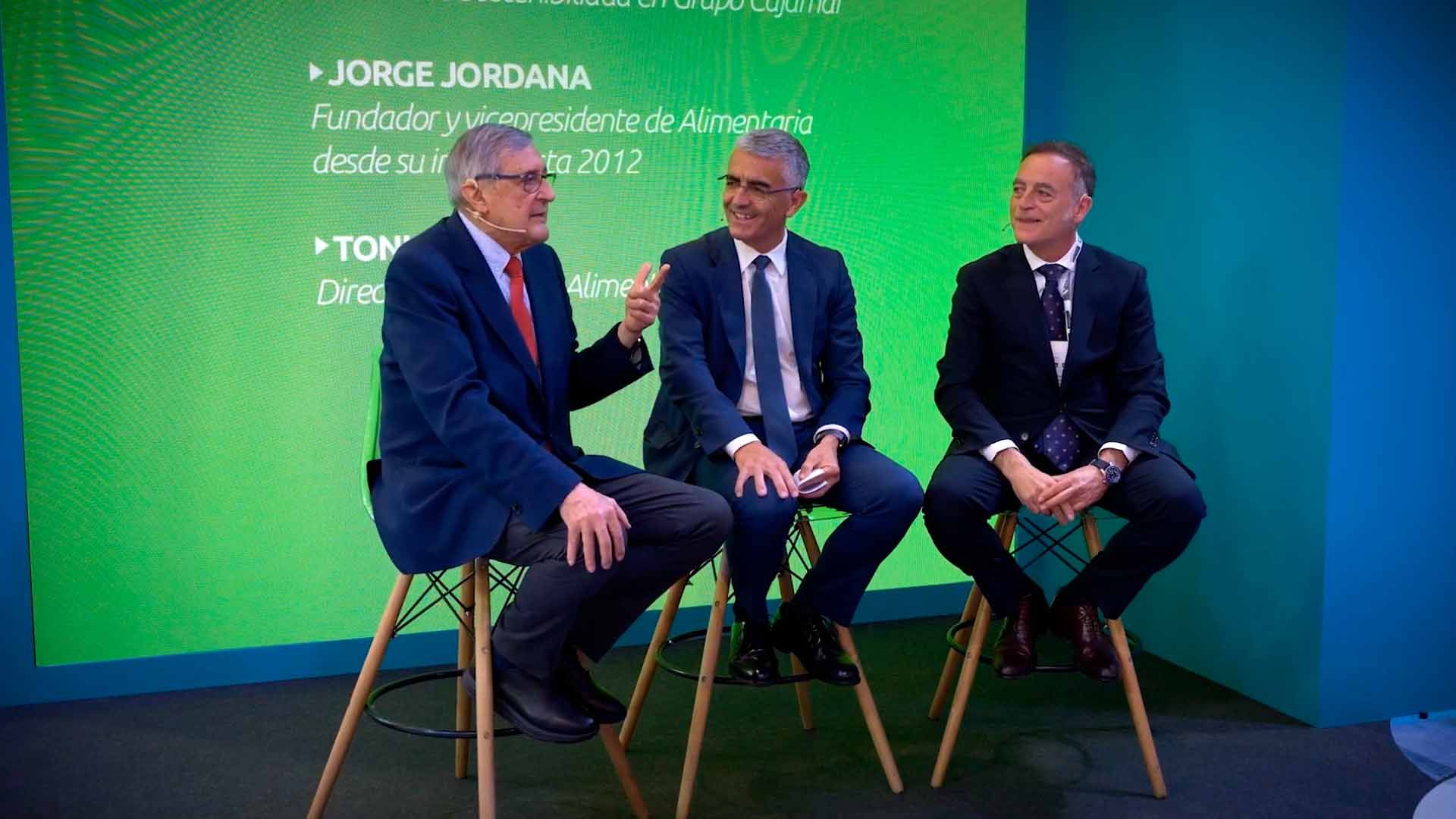 La imagen muestra a tres hombres sentados en taburetes con un panel verde detrás.