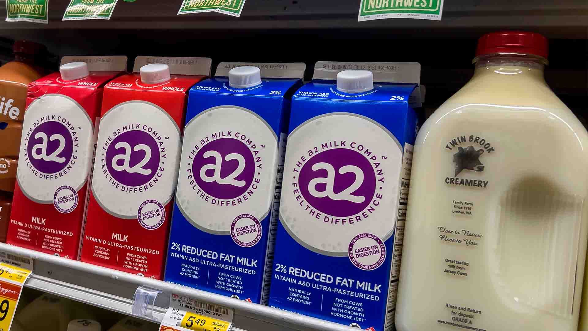 Cartones y botella de leche de diferentes marcas en un estante de supermercado.