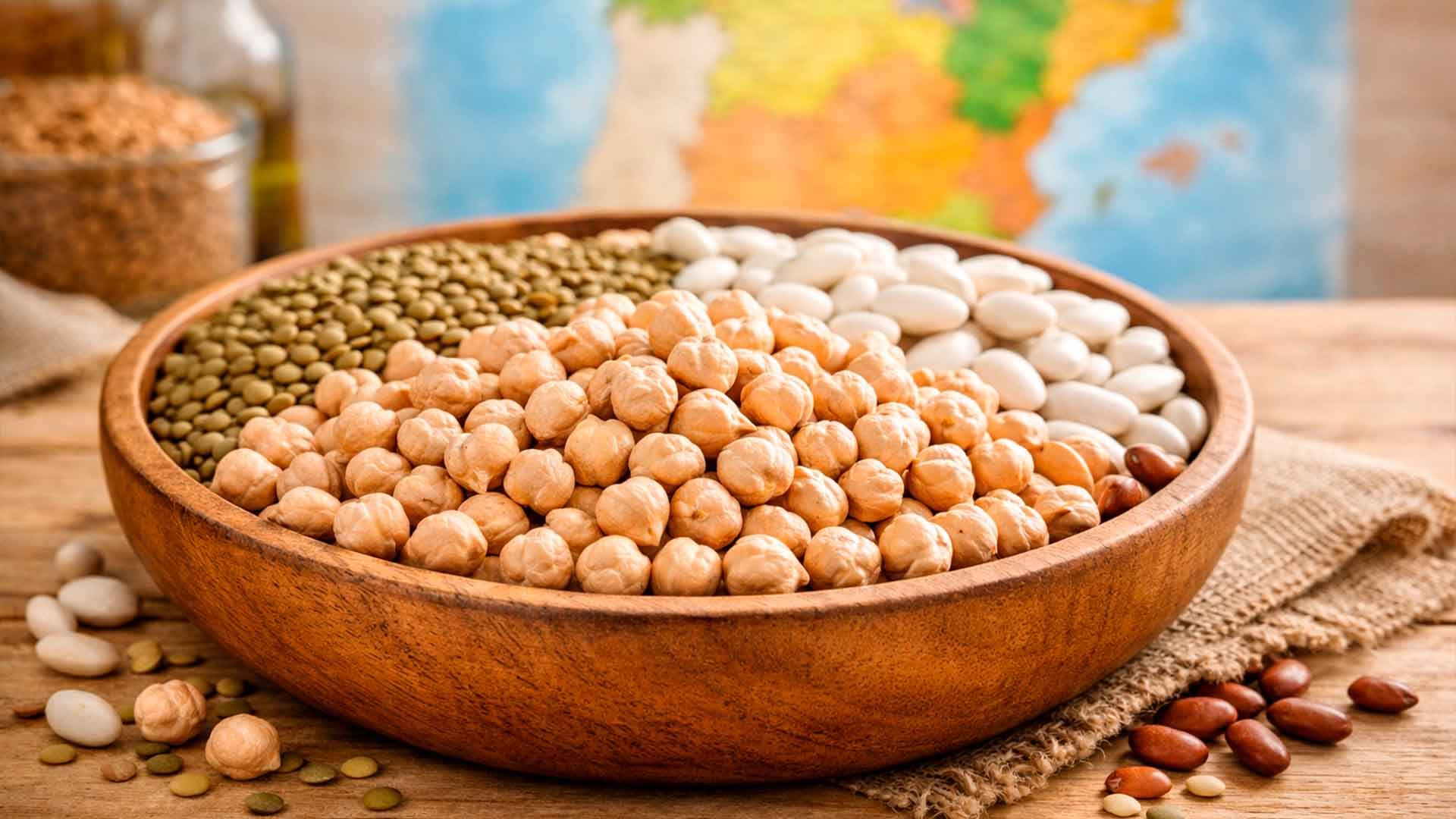 Copa de madera con lentejas, frijoles y garbanzos en una mesa rústica.