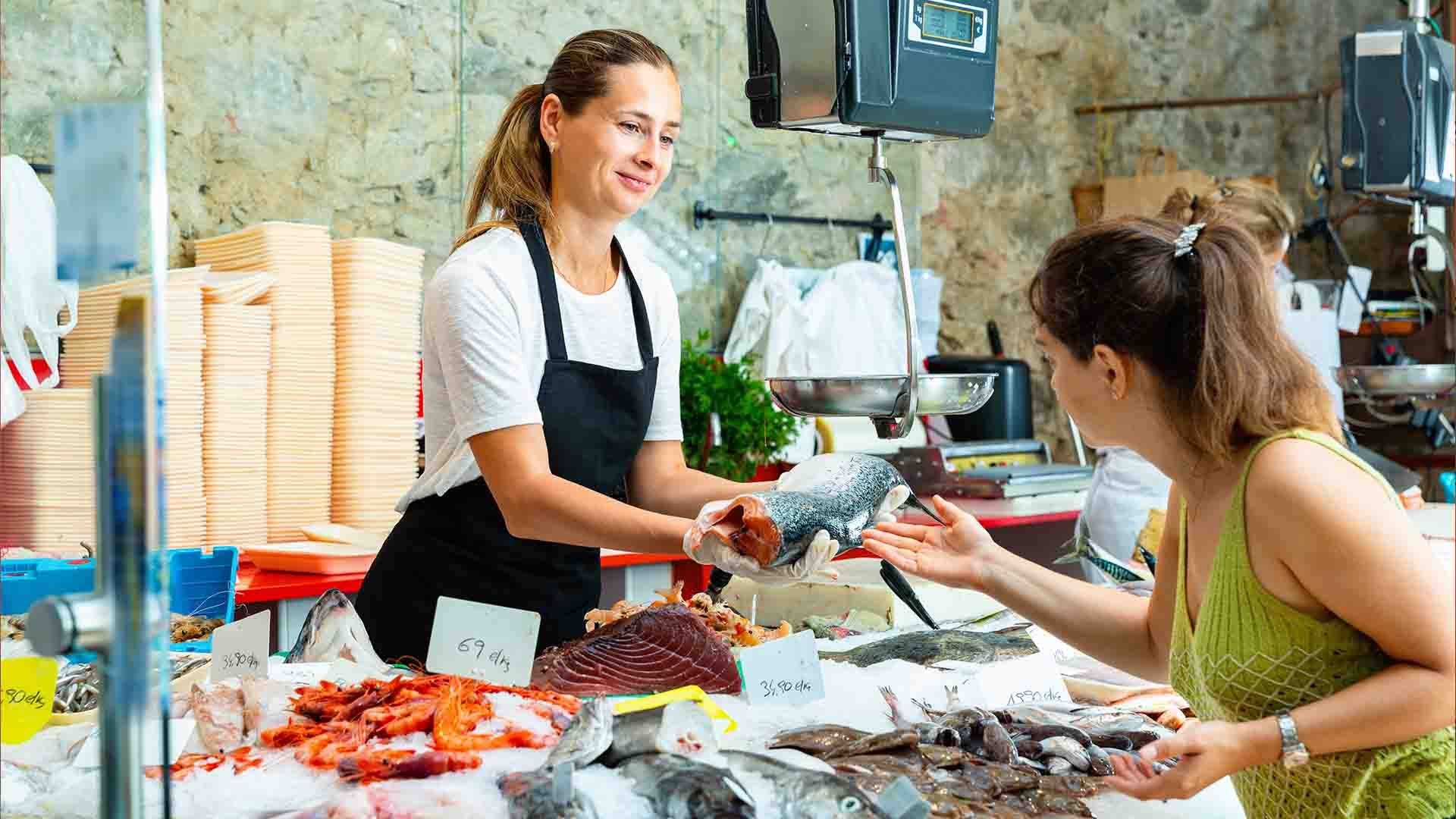 Una mujer compra un pescado a una vendedora en un mercado de pescado.