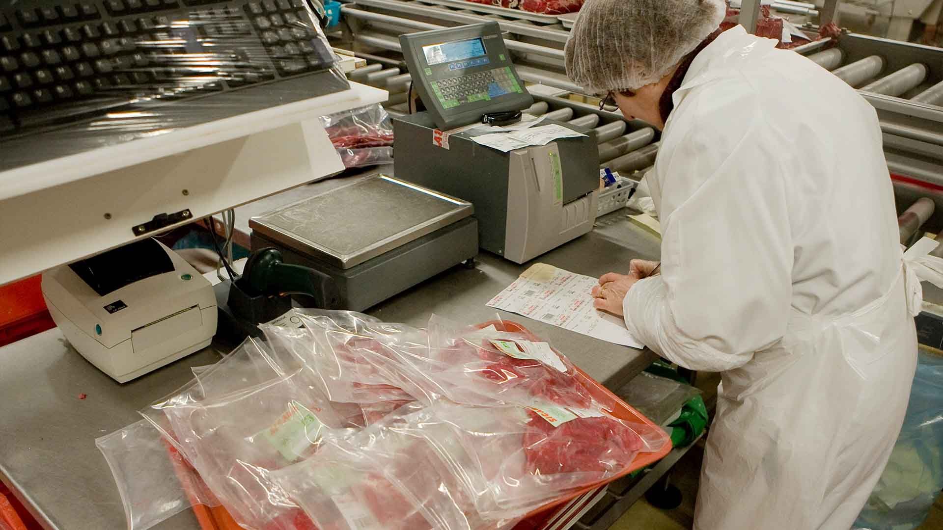 La imagen muestra a una mujer operando en una planta procesadora de carne.