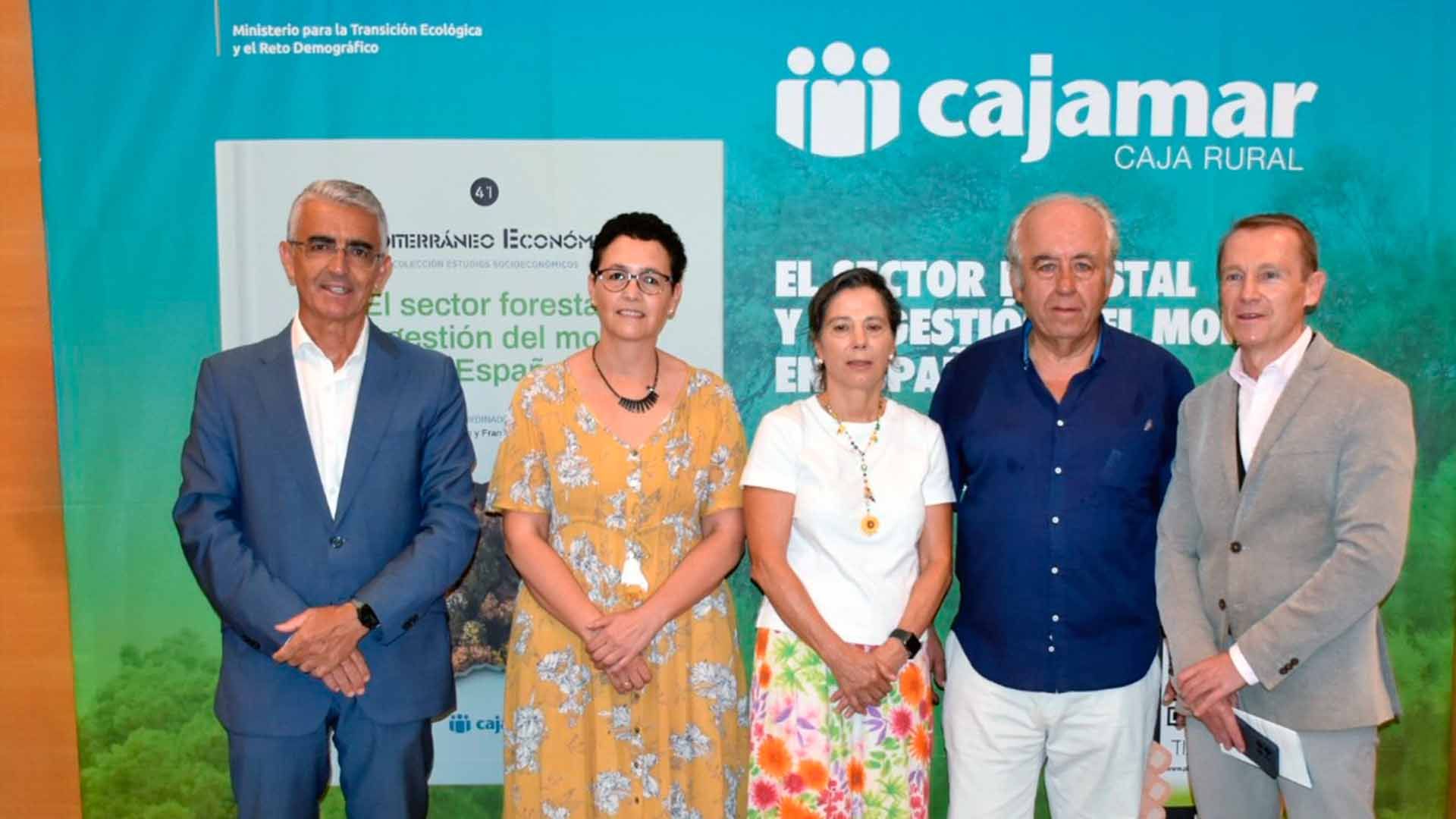 Cinco personas posan ante un cartel en un evento, sonriendo y vestidos formalmente.