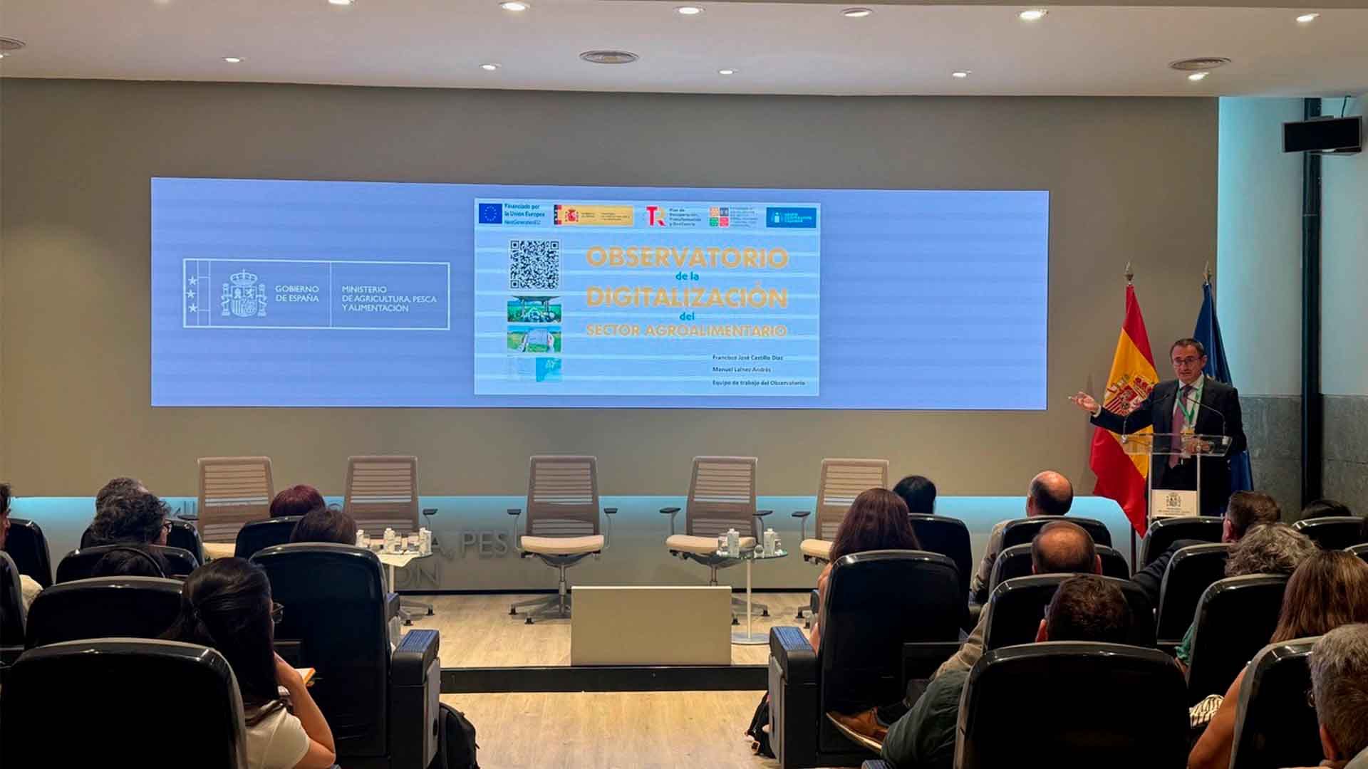 Un hombre habla en una conferencia con público y una pantalla detrás de él.