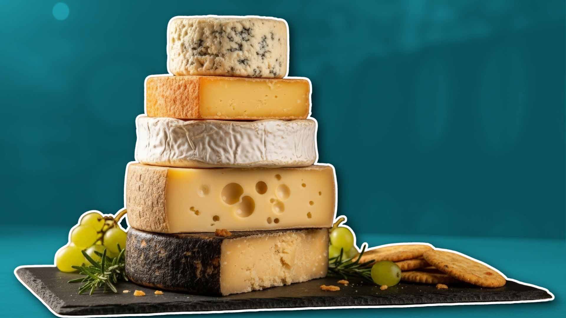 Una pirámide de varios tipos de queso con uvas y galletas en una tabla.