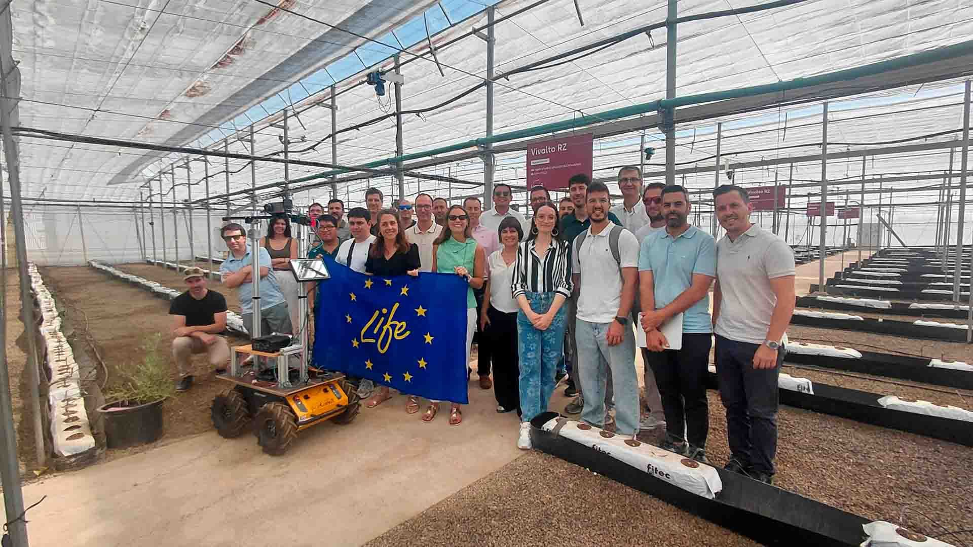 Grupo de personas con una bandera de la Unión Europea en un invernadero.