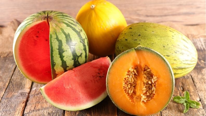 Sandías y melones enteros y cortados sobre una mesa de madera, mostrando su pulpa roja y anaranjada, ilustrando la campaña 2026 de estas frutas de verano