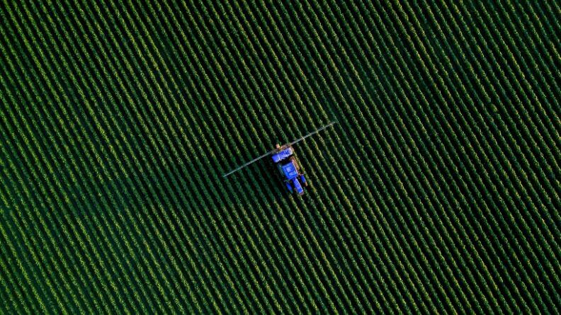 Vista de pájaro de un cultivo al aire libre con un tractor en el centro, sistema agroalimentario mundial