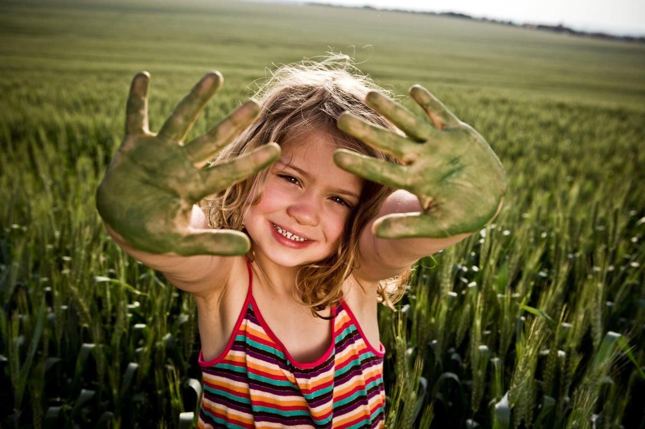 Niña en un campo de trigo mostrando a cámara las palmas de las manos pintadas de verde